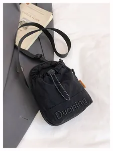 Detail of black crossbody bag featuring 3D embossed lettering and orange side label detail