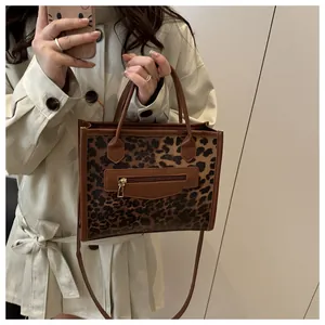 Detail of leopard print tote bag featuring brown leather trim and front zipper pocket