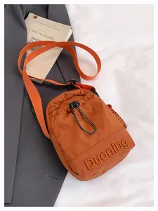 Orange nylon crossbody bag with Duoning embroidery and adjustable strap on white sheets