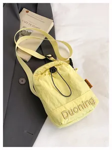 Detail of light yellow nylon crossbody bag with side orange ribbon on grey suit background