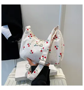 Detailed view of white corduroy shoulder bag featuring a red cherry pattern print