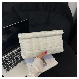 Close-up of white quilted puffer envelope bag with gold hardware on a desk