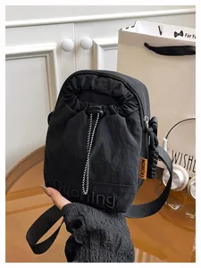 Detail of black nylon crossbody bag with drawstring, orange fashion label, and wide strap