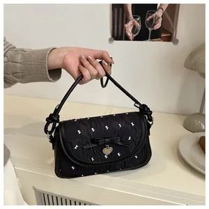 Close-up of bow detailing and heart pendant on black pleated luxury handbag