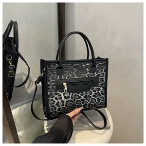 Detail of grey leopard print tote bag featuring black leather handles and front zip pocket