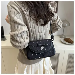 Detailed view of black pleated handbag with bow, heart pendant and white embroidery detail