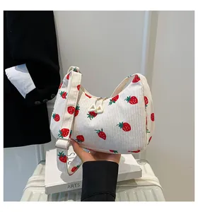 Detail of white corduroy dumpling bag featuring red strawberry prints and zipper closure