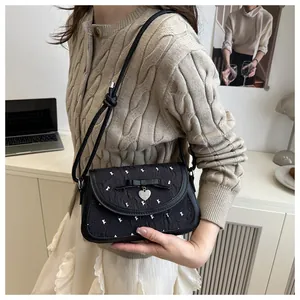 Detail of crossbody bag featuring a black bow, silver heart charm and bow shoulder strap