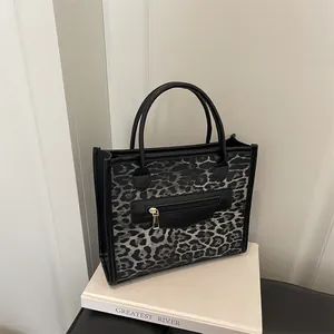 Chic leopard print handbag with black leather handles and front zipper on a minimalist stand
