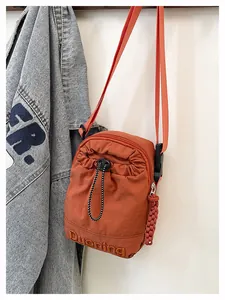 Close-up of orange-red nylon crossbody bag with drawstring pocket and woven zipper pull