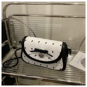 Macro detail of white pleated crossbody bag with black bow prints and heart pendant