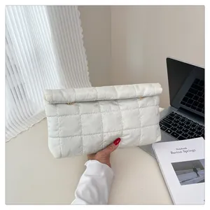 Detail shot of white quilted envelope clutch bag with gold clasp on office desk scene