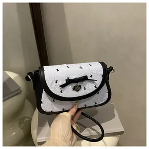 Detailed close-up of a white textured crossbody bag with black bow and heart pendant