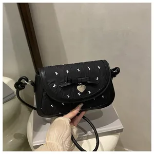 Detail of black quilted shoulder bag featuring white bow patterns and a silver heart charm