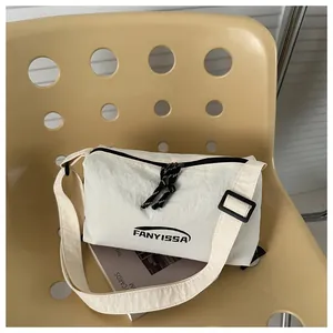 Détail du sac bandoulière blanc cassé en tissu texturé avec logo FANYISSA posé sur une chaise