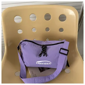 Détail du petit sac bandoulière en nylon violet avec logo blanc et bandoulière rayée décor