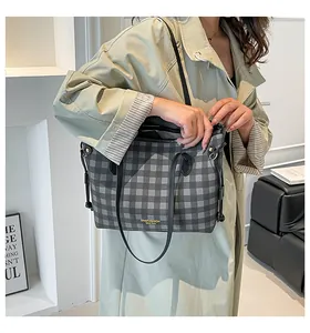 Grey checkered tote bag detail showing black leather handles and adjustable strap on model