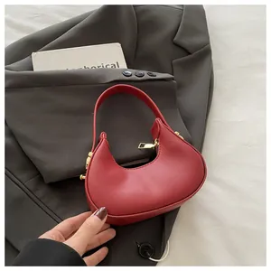 Detail of red mini crescent handbag with gold zipper and metal studs on grey background