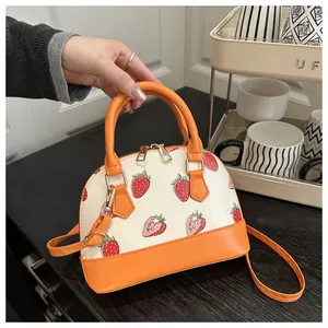 Detail of strawberry print crossbody bag with orange trim and gold-tone hardware