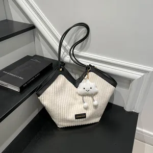 Chic cream and black corduroy tote bag with plush charm on minimalist background