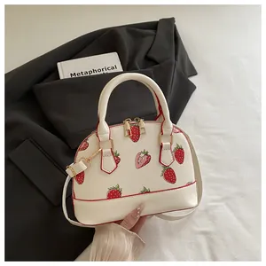 Detail of white shell bag with strawberry print, red piping and gold hardware