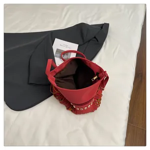 Détail d'un sac seau rouge en PU avec glands en cuir, rivets dorés et intérieur zippé