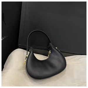 Detail of a black crescent mini handbag with gold metal buckles on white fabric
