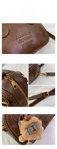 Detailed close-up of brown leather bag with embossed logo, metal zipper, and plush charm