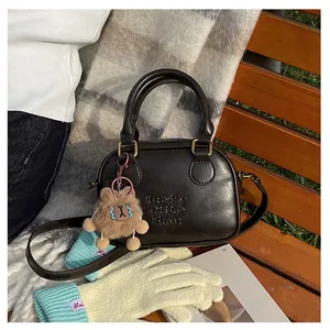 Detail of dark brown leather crossbody bag with teddy bear charm on a park bench