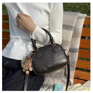 Detailed shot of dark brown crossbody bag with embossed text and plush animal charm