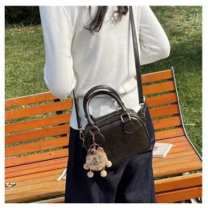 Outdoor view of a dark brown crossbody bag with a plush bear charm and letter detail