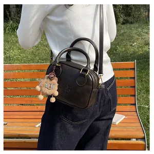 Detail of dark brown leather crossbody bag with cute lion pendant on wooden bench