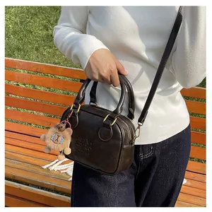 Detail of dark brown faux leather mini tote bag featuring embossed logo and cute bear charm