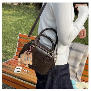 Detail of dark brown square crossbody bag with plush bear charm and matte leather texture
