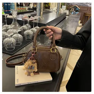 Detail view of retro brown Boston bag with embossed text and plush bear charm