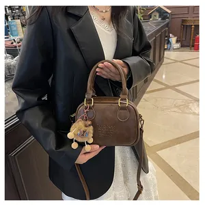 Close-up of brown PU leather handbag featuring a plush lion charm and embossed logo detail