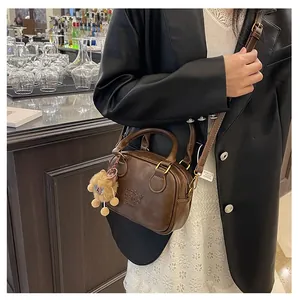 Detail of dark brown leather handbag with LUCKY CHILD embossing and plush bear charm