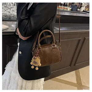 Detail of dark brown leather Boston bag with embossed logo and plush bear charm
