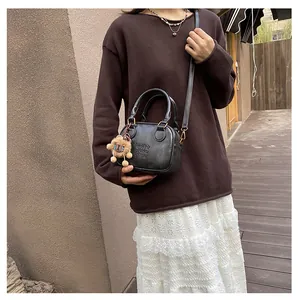 Detail of a black mini square bag with leather texture and cute plush bear charm accessory