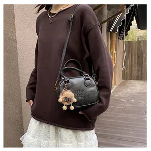 Close-up of black matte crossbody bag with embossed lettering and a cute bear charm