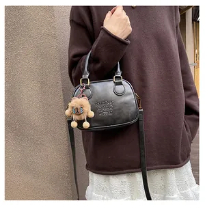Detail of black crossbody bag with letter embossing and cute brown bear plush charm