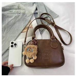 Detail view of small brown crossbody bag with plush lion charm and smartphone for scale