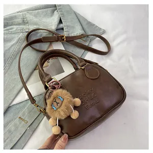 Detail of dark brown leather crossbody bag featuring a cute plush lion charm and embossed logo