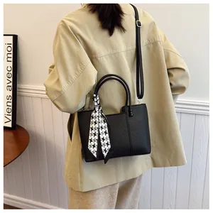 Détail du sac à main en cuir grainé noir avec un foulard décoratif en soie à motif géométrique