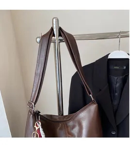 Détail du sac croissant marron foncé avec breloque tressée rouge et blanche sur la fermeture