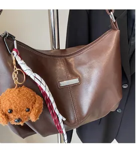 Gros plan sur un sac hobo en cuir marron avec breloque chien et détails de sangle tressée