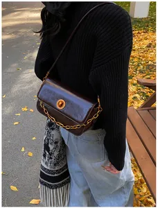 Macro detail of dark brown leather shoulder bag with golden round lock and chunky chain