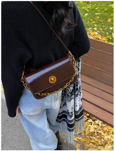Detail of a dark brown glossy leather shoulder bag with golden chain and metal turn lock