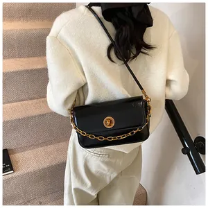 Detailed shot of a black glossy shoulder bag featuring a bold gold chain and circular metal lock