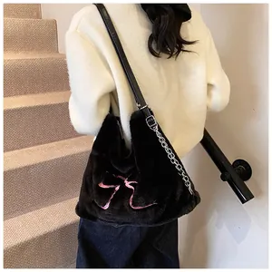 Dettaglio della borsa tote in peluche nera con fiocco rosa e tracolla a catena in metallo
